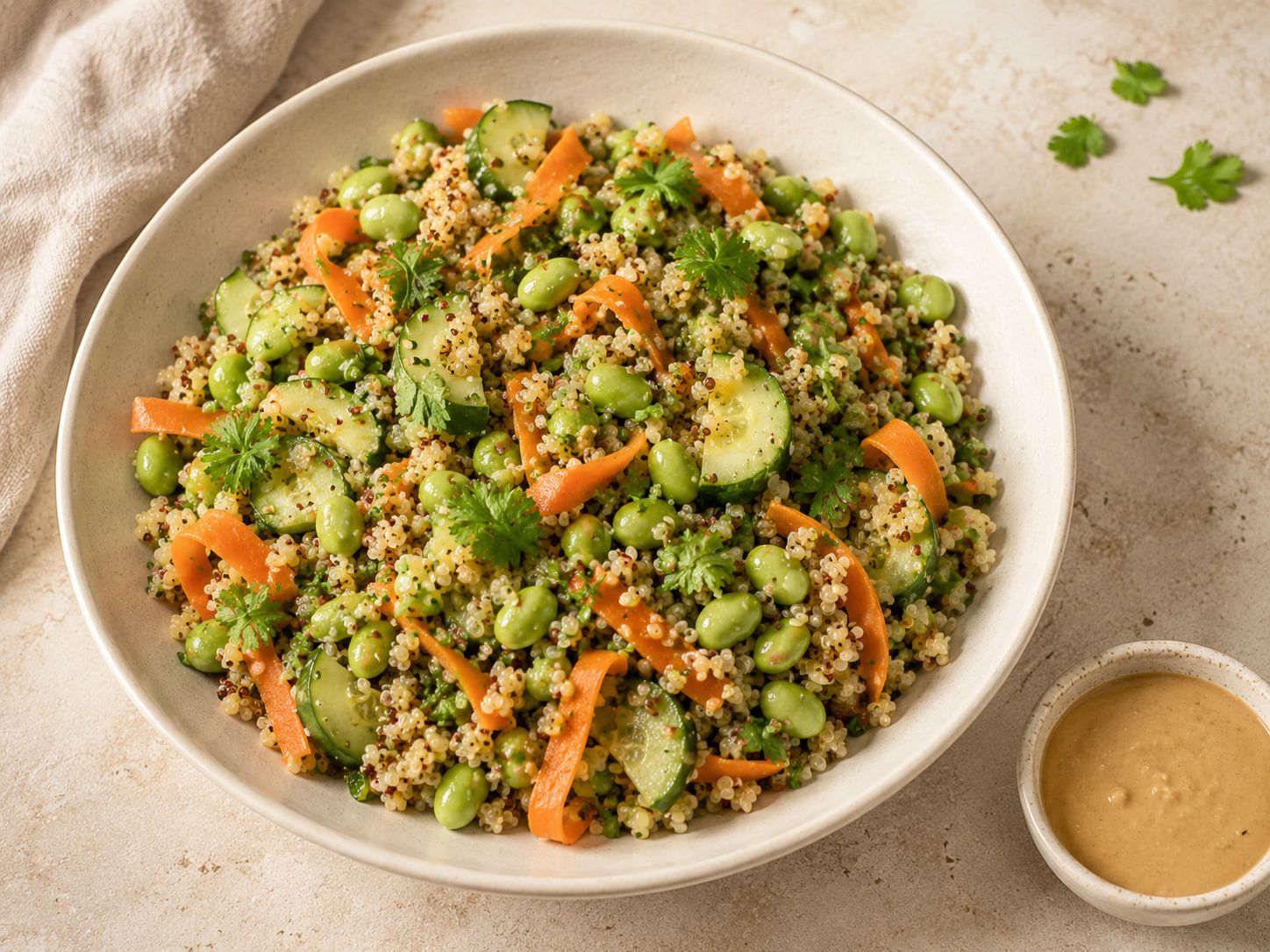 Bol de quinoa con edamame, pepino y tiras de zanahoria, con un cuenco de salsa de cacahuete.